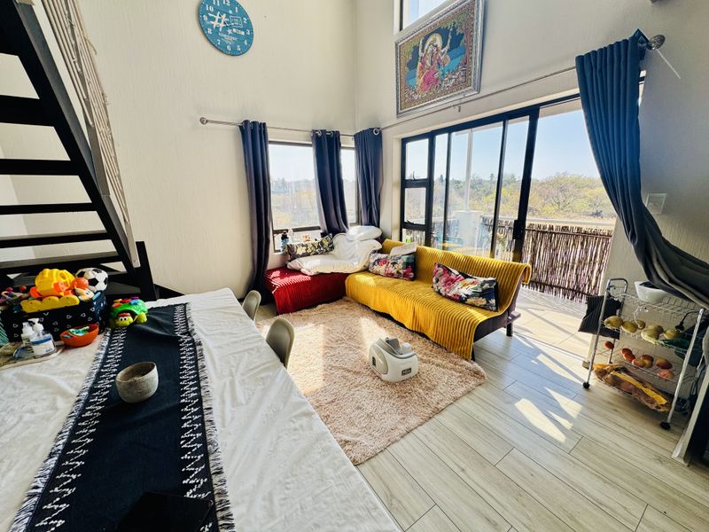 Bright open-plan living area featuring double volume ceilings, tiled flooring, and large sliding glass doors leading to an outdoor balcony space.