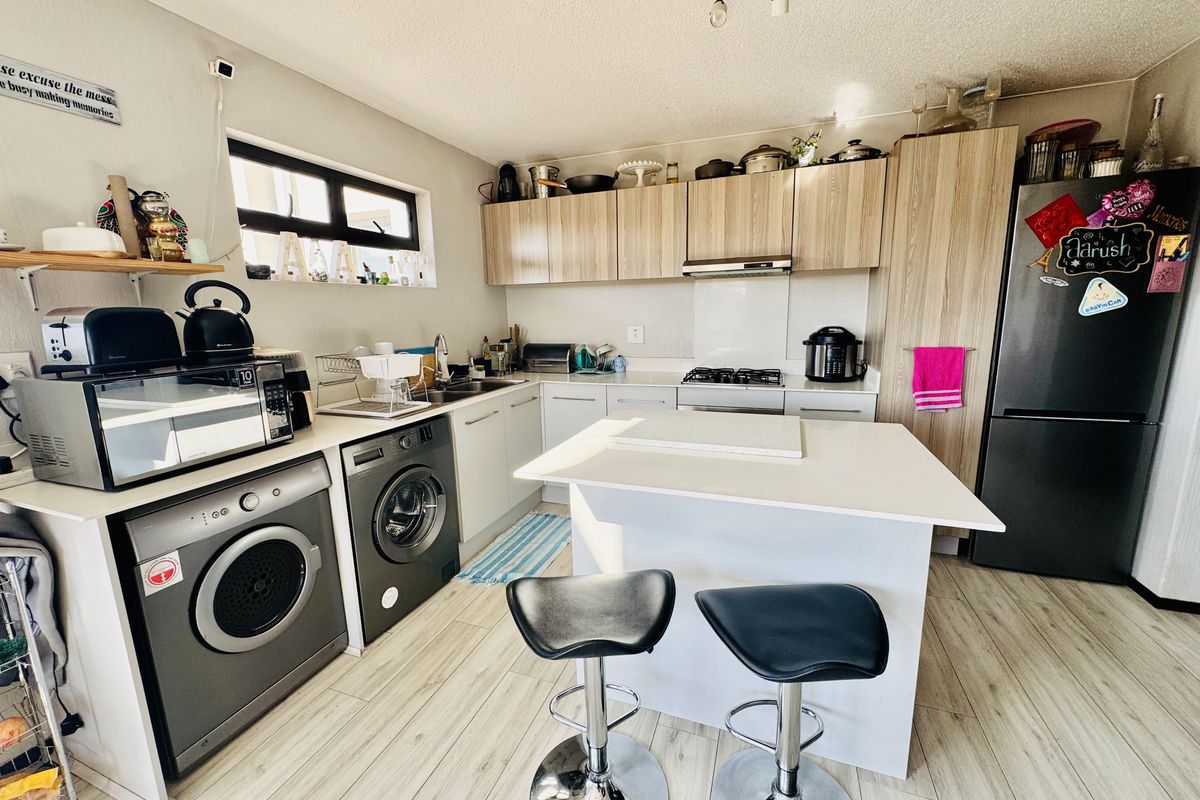 A functional kitchen featuring light wood-tone cabinetry, laminate countertops, a central island, and integrated laundry appliances, offering a practical layout for daily use.