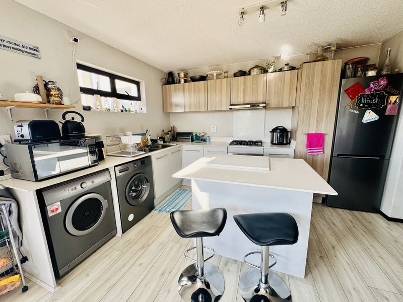A functional kitchen featuring light wood-tone cabinetry, laminate countertops, a central island, and integrated laundry appliances, offering a practical layout for daily use.