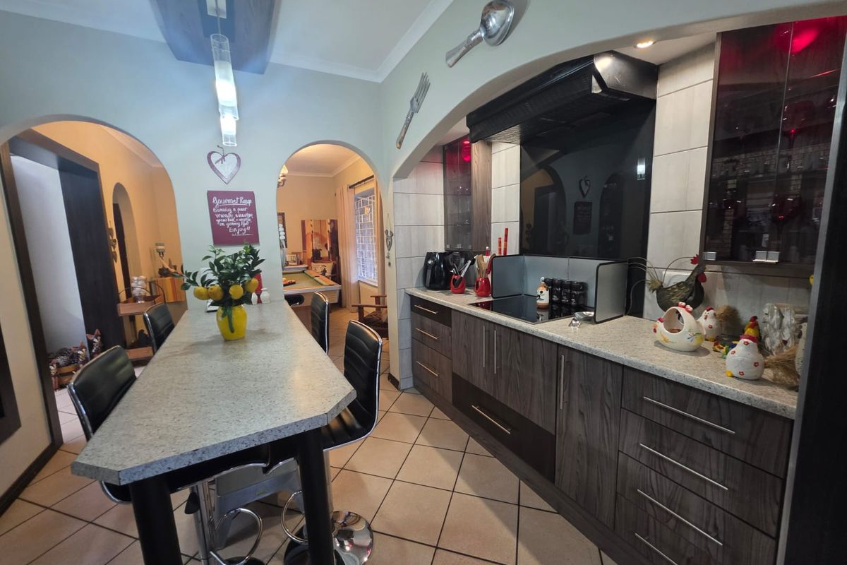 A functional kitchen featuring modern dark wood cabinetry, stone-look countertops, an integrated hob with extractor, and tiled flooring, connected via open archways.