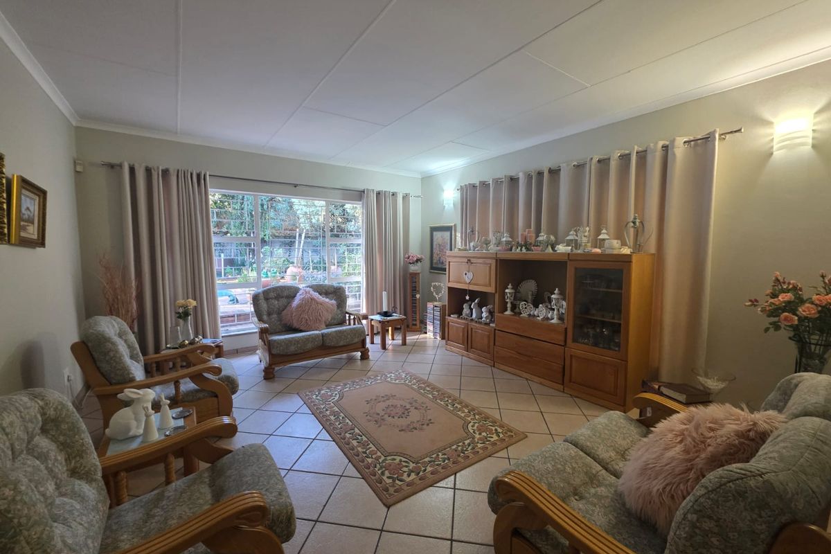 A spacious living room featuring tiled flooring and large windows that provide natural light and a view of the outdoor area.