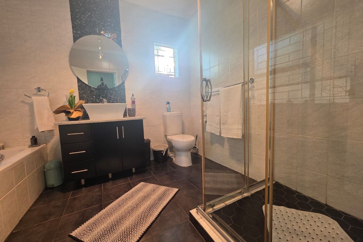 A modern bathroom featuring a dark vanity cabinet, vessel sink, glass-enclosed shower, and a built-in bathtub with neutral wall tiling.