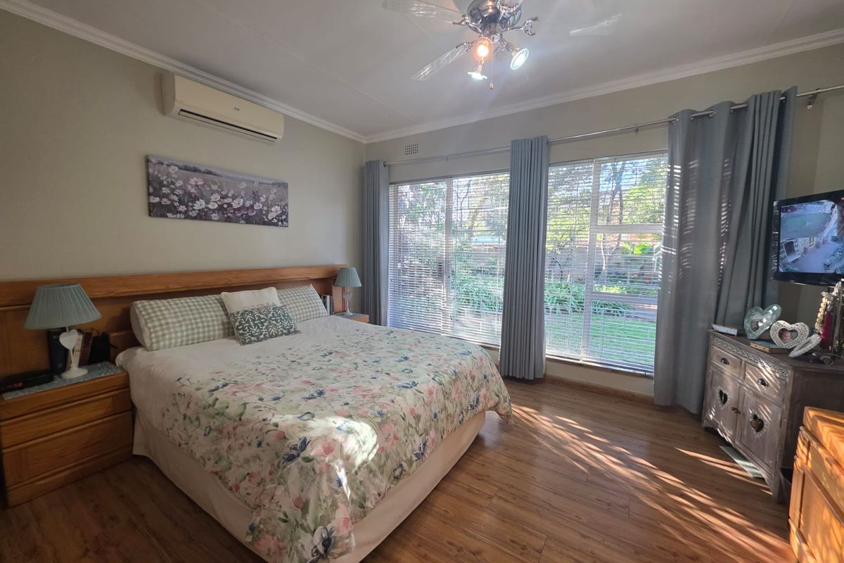 A well-maintained bedroom featuring laminate flooring, a ceiling fan, a split-system air conditioner, and large windows overlooking the garden.