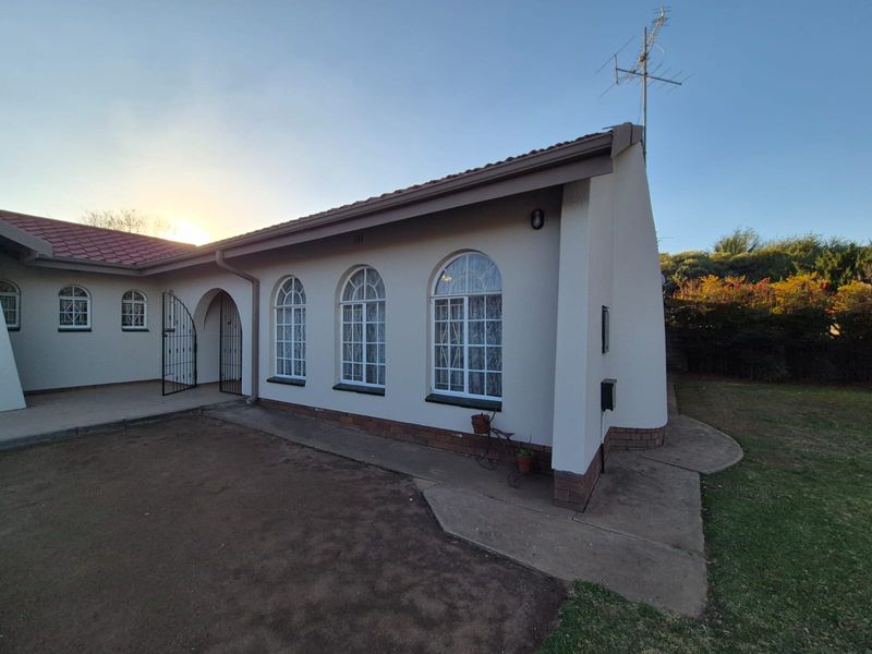 Rear view of the house featuring arched windows, a tiled roof, and a concrete pathway leading along the exterior wall.