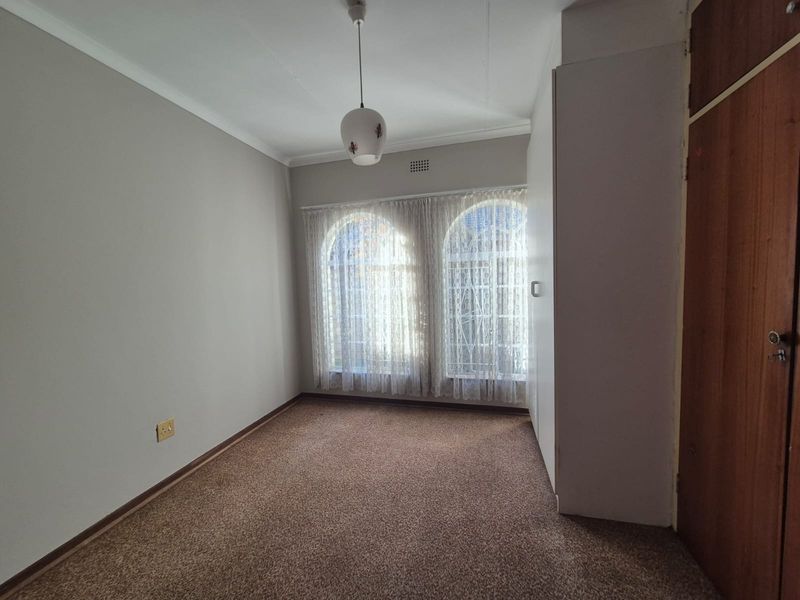 A vacant bedroom featuring carpeted flooring, built-in cupboards, and distinctive arched windows, offering a neutral canvas for personalization.