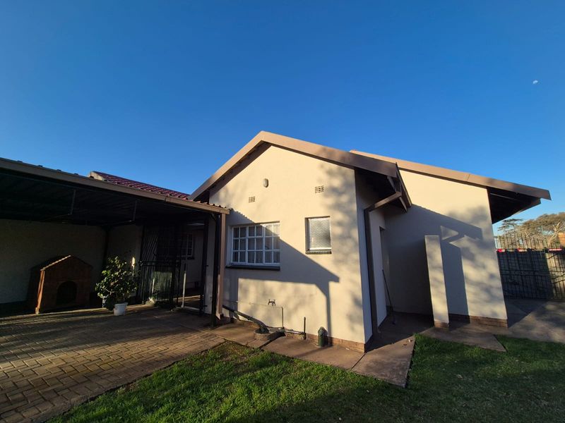 Rear view of the property featuring a paved patio area, attached carport, and well-maintained exterior walls with functional guttering.