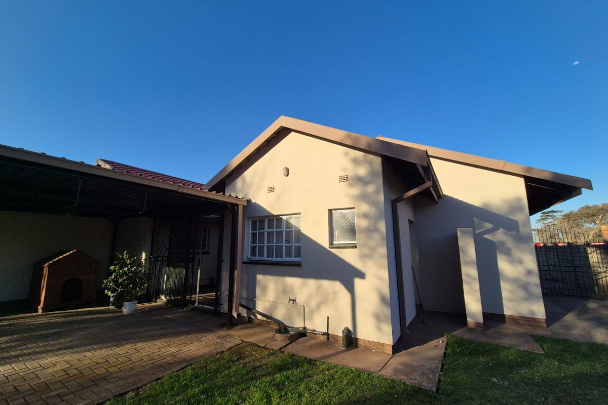 Rear view of the property featuring a paved patio area, attached carport, and well-maintained exterior walls with functional guttering.