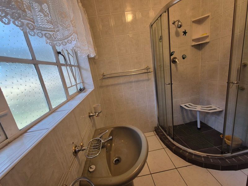 A functional bathroom featuring a corner shower enclosure with a built-in seat, pedestal basin, and neutral wall tiling.
