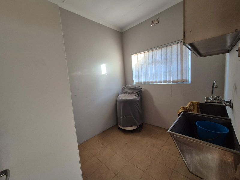 A functional laundry room featuring a stainless steel trough, tiled flooring, and a window with vertical blinds.