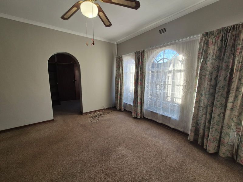 A spacious bedroom featuring arched windows, a ceiling fan, and an arched doorway leading to an adjacent area, finished with neutral wall tones.