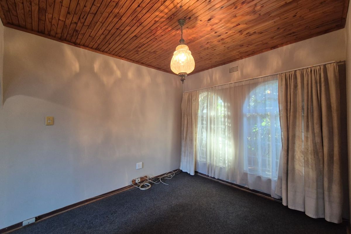 An empty living room featuring a timber tongue and groove ceiling, arched windows with security bars, and carpet flooring.