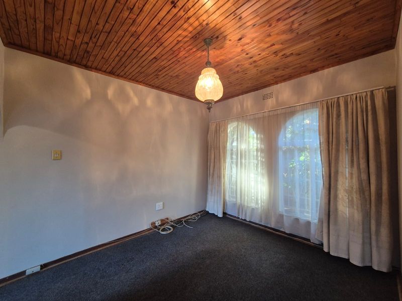 An empty living room featuring a timber tongue and groove ceiling, arched windows with security bars, and carpet flooring.