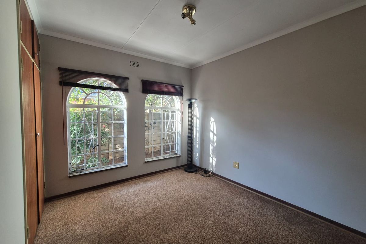 A spacious, empty bedroom featuring built-in cupboards, arched windows with security bars, and neutral carpeting, offering a blank canvas for personalization.