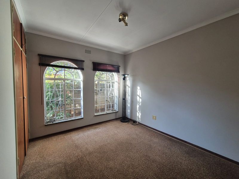 A spacious, empty bedroom featuring built-in cupboards, arched windows with security bars, and neutral carpeting, offering a blank canvas for personalization.