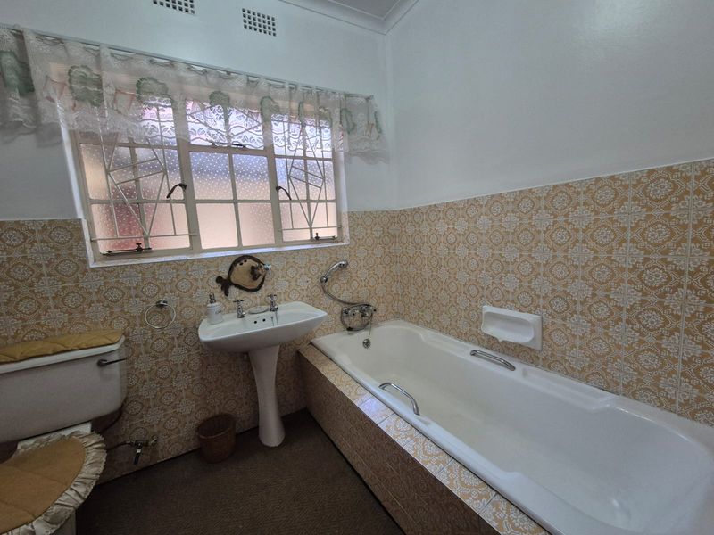 A dated bathroom featuring a pedestal basin, built-in bathtub, and patterned wall tiles, offering significant potential for a modern renovation.