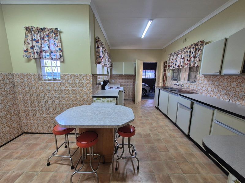 A dated kitchen featuring original cabinetry, tiled splashbacks, and a central breakfast nook, offering significant potential for a modern renovation.