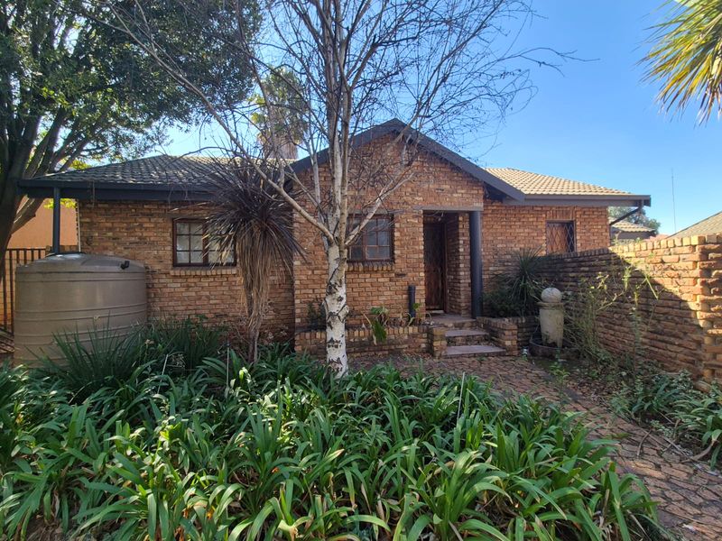 A face brick exterior featuring a tiled roof, paved entrance path, and a water storage tank, set within a mature garden environment.
