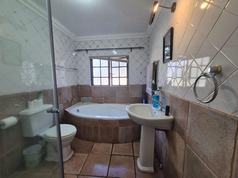 A dated bathroom featuring a pedestal basin, built-in bathtub, and a glass-enclosed shower with traditional ceramic tiling.