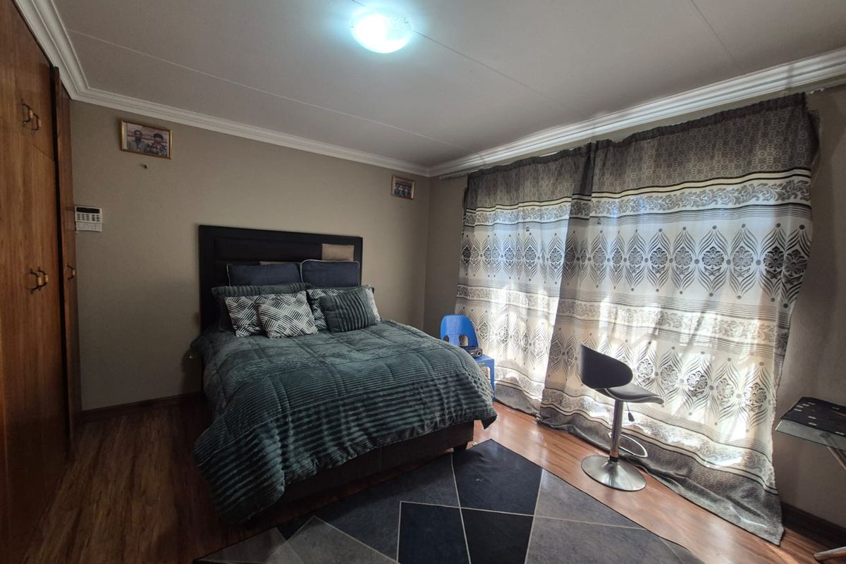 A bedroom featuring laminate flooring, built-in cupboards, and ceiling cornicing, offering a functional space with natural light through large window coverings.