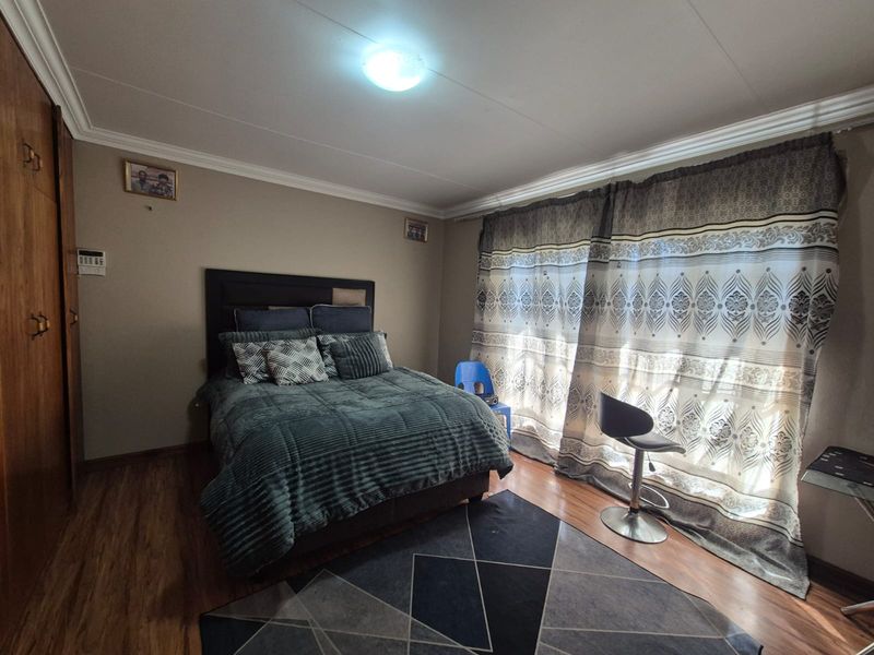 A bedroom featuring laminate flooring, built-in cupboards, and ceiling cornicing, offering a functional space with natural light through large window coverings.