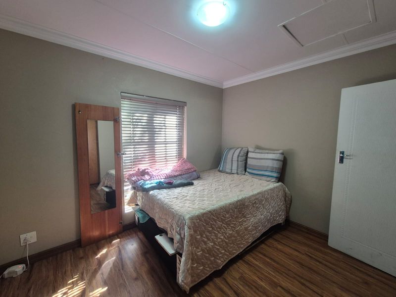 A functional bedroom featuring laminate flooring, neutral wall tones, and a window fitted with venetian blinds, providing a simple and comfortable living space.