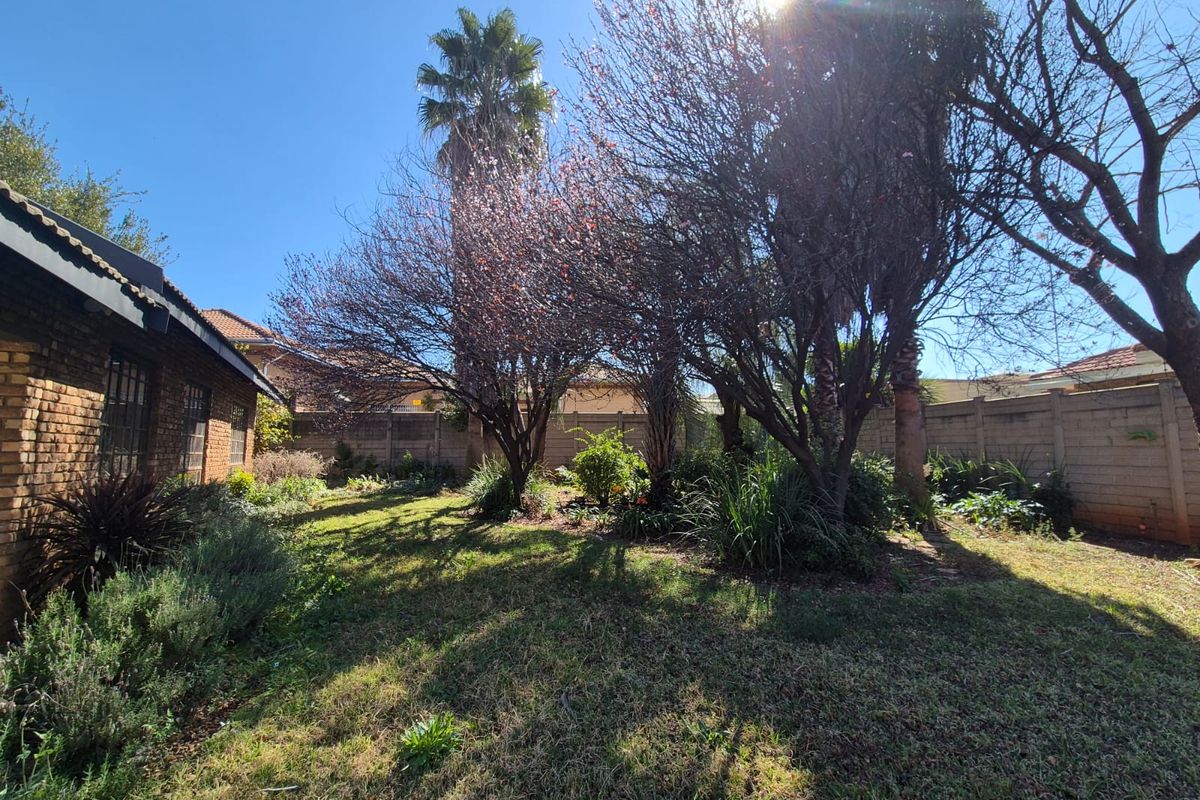 A private rear garden featuring established trees, a lawn area, and secure brick boundary walls.