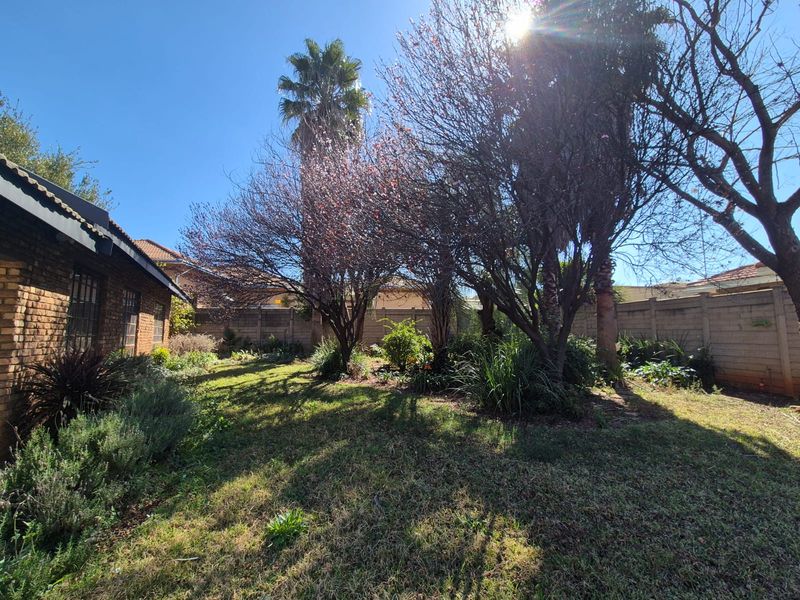 A private rear garden featuring established trees, a lawn area, and secure brick boundary walls.