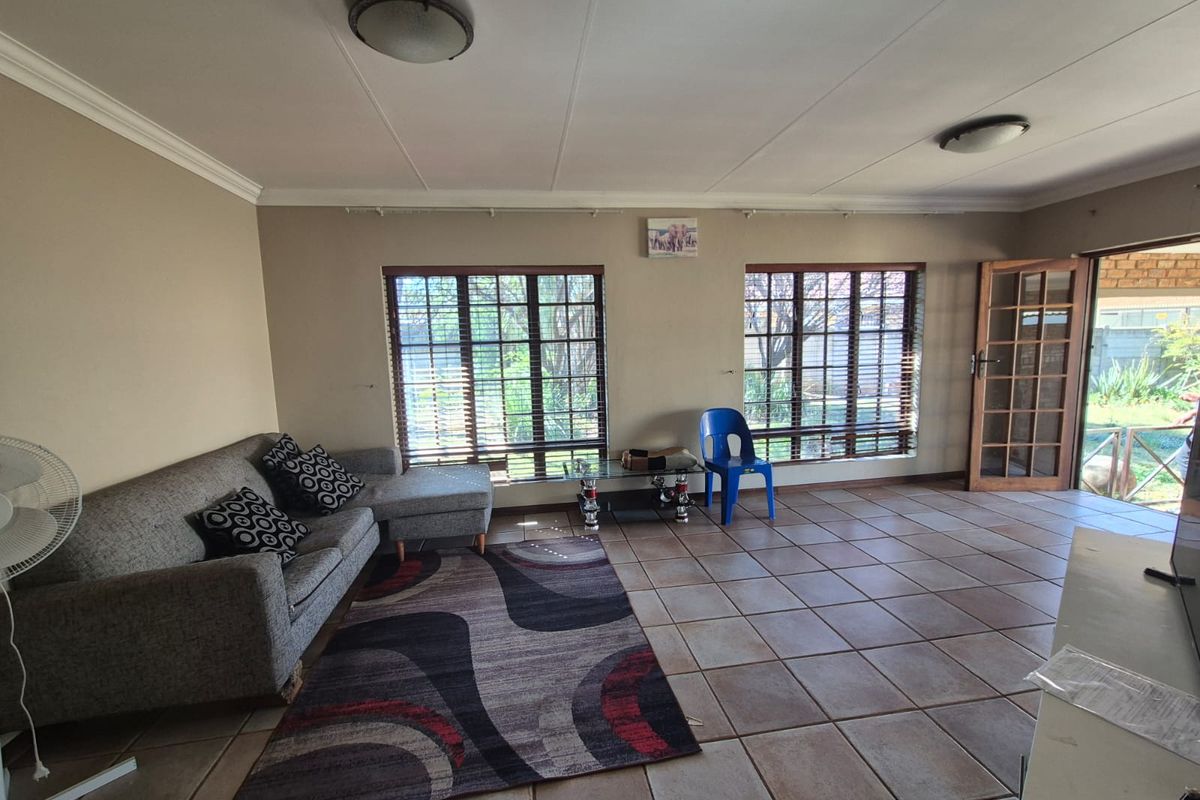 Spacious living room featuring tiled flooring, large windows with venetian blinds, and direct access to the outdoor area through a timber-framed glass door.