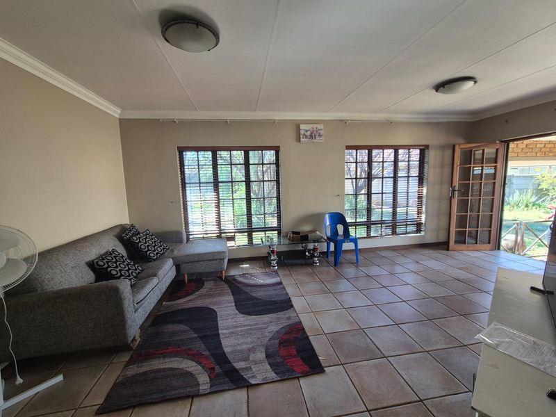 Spacious living room featuring tiled flooring, large windows with venetian blinds, and direct access to the outdoor area through a timber-framed glass door.