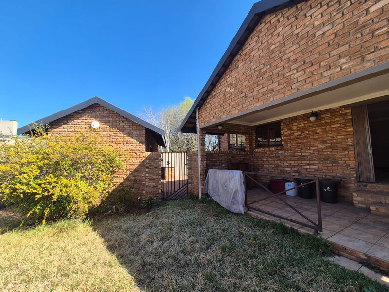 Rear view of the property featuring a face brick facade, a covered patio area, and a small garden space with a secure gate.