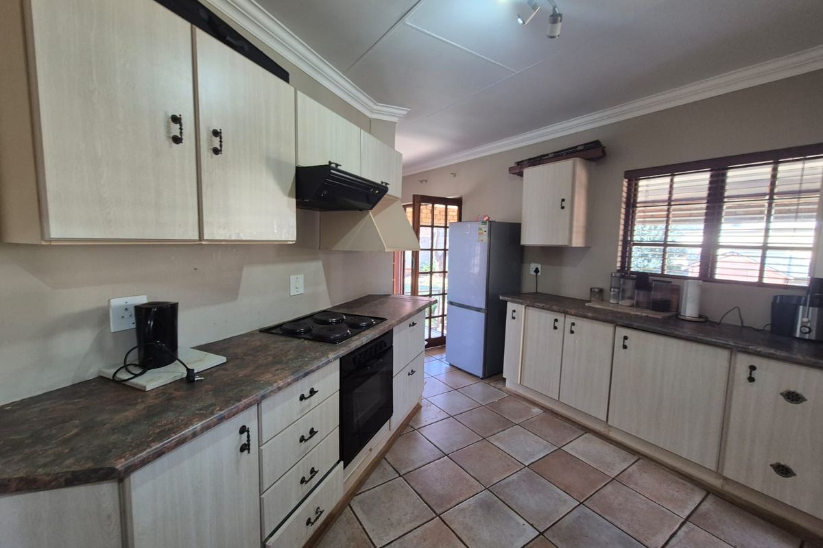 A functional kitchen featuring light-toned laminate cabinetry, dark countertops, built-in oven and hob, and tiled flooring with direct access to the outdoor area.