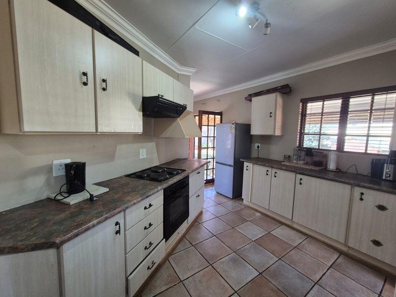 A functional kitchen featuring light-toned laminate cabinetry, dark countertops, built-in oven and hob, and tiled flooring with direct access to the outdoor area.