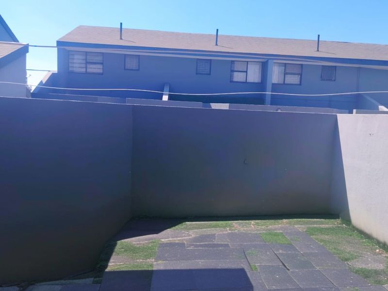 A rear exterior view of the townhouse featuring a private paved courtyard area enclosed by boundary walls.