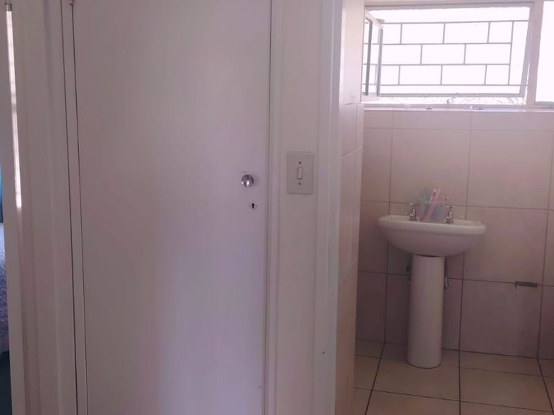 A functional bathroom featuring a pedestal basin, tiled walls and flooring, and a built-in storage cupboard with security bars on the window.