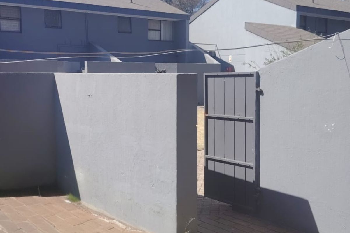 A paved rear patio area featuring a boundary wall and a metal pedestrian gate, providing access to the outdoor space.