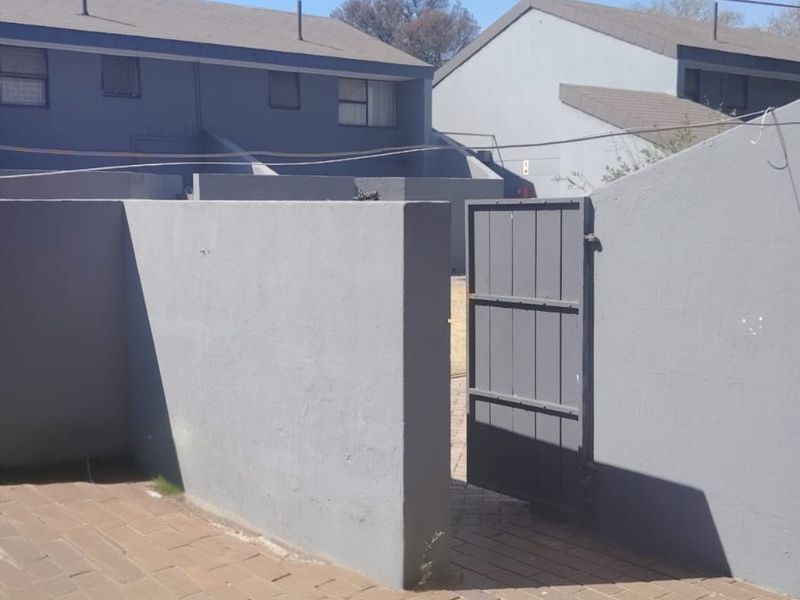 A paved rear patio area featuring a boundary wall and a metal pedestrian gate, providing access to the outdoor space.