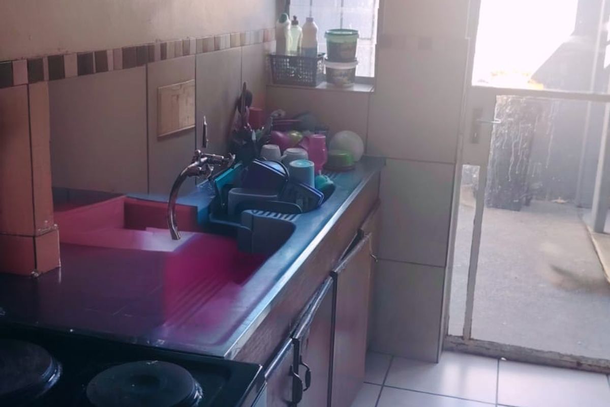 A compact kitchen featuring tiled flooring, built-in cabinetry, a sink, and direct access to an outdoor area through a security gate.