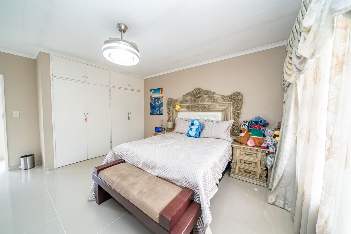 A well-maintained bedroom featuring neutral tiled flooring, built-in storage cupboards, and a modern ceiling fan with integrated lighting.