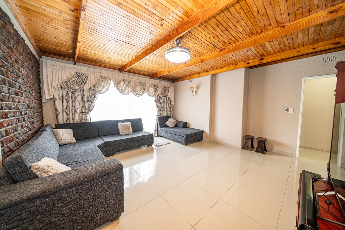 Spacious living room featuring a distinctive timber tongue and groove ceiling, polished porcelain floor tiles, and a rustic exposed brick feature wall.
