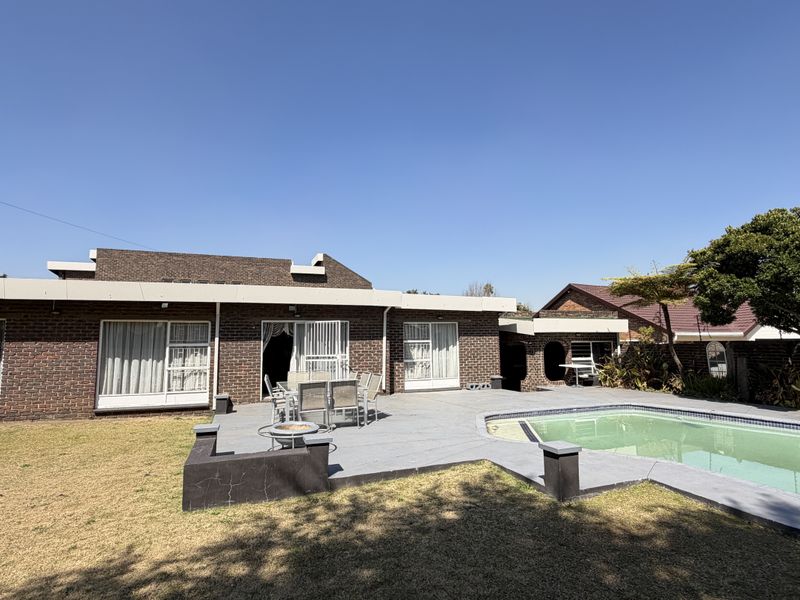 Rear exterior view featuring a brick house, a paved patio area, and a swimming pool set within a garden.