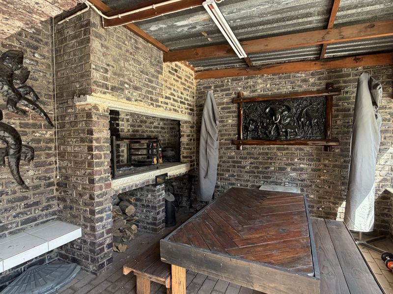 Covered outdoor patio area featuring a built-in brick braai, exposed brick walls, and timber roof beams, providing a rustic entertainment space.