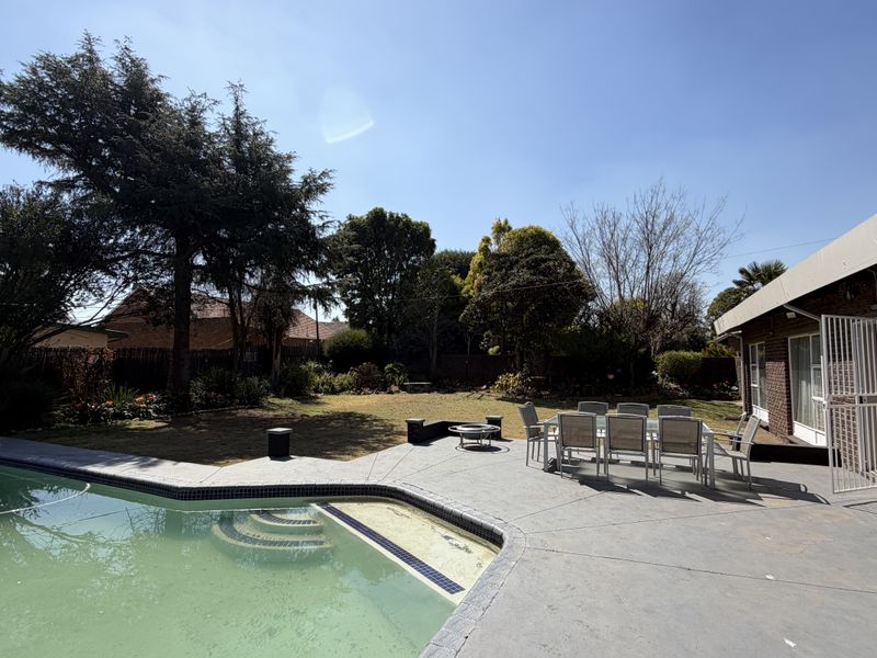 Outdoor entertainment area featuring a swimming pool and a spacious concrete patio adjacent to the brick house exterior.