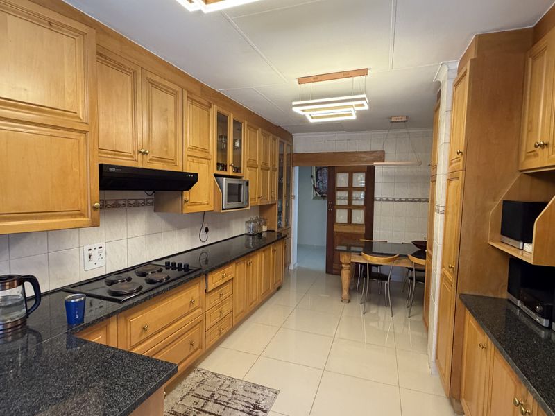 A functional kitchen featuring extensive wooden cabinetry, granite countertops, an integrated hob, and tiled flooring, offering a classic and well-maintained workspace.