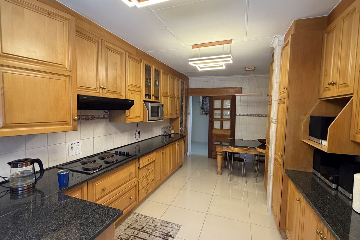 A functional kitchen featuring extensive wooden cabinetry, granite countertops, an integrated hob, and tiled flooring, offering a classic and well-maintained workspace.