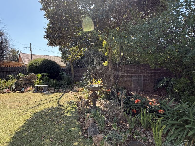 A private rear garden featuring a lawn, established trees, a brick boundary wall, and a stone bird bath.