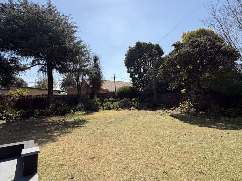 A spacious, well-established private garden featuring a large lawn area, mature trees, and secure boundary fencing.