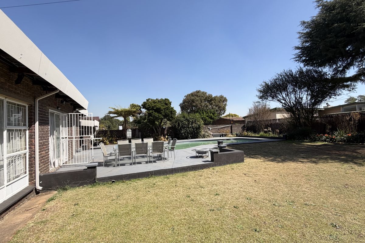 Rear exterior view featuring a paved patio area, swimming pool, and established garden with brick building facade.