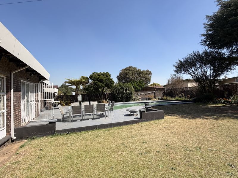 Rear exterior view featuring a paved patio area, swimming pool, and established garden with brick building facade.