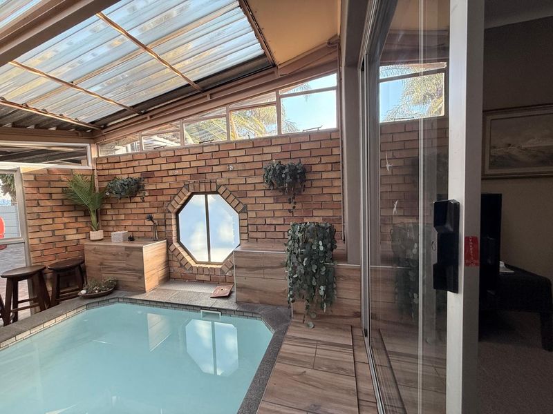 An indoor swimming pool area featuring exposed brick walls, an octagonal window, and a translucent roof, connected to the main living space via sliding doors.