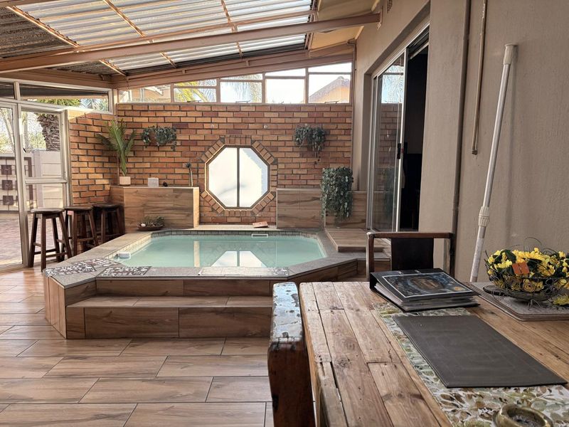 Covered patio area featuring a built-in indoor swimming pool, exposed brick feature wall, octagonal window, and modern wood-look floor tiles.